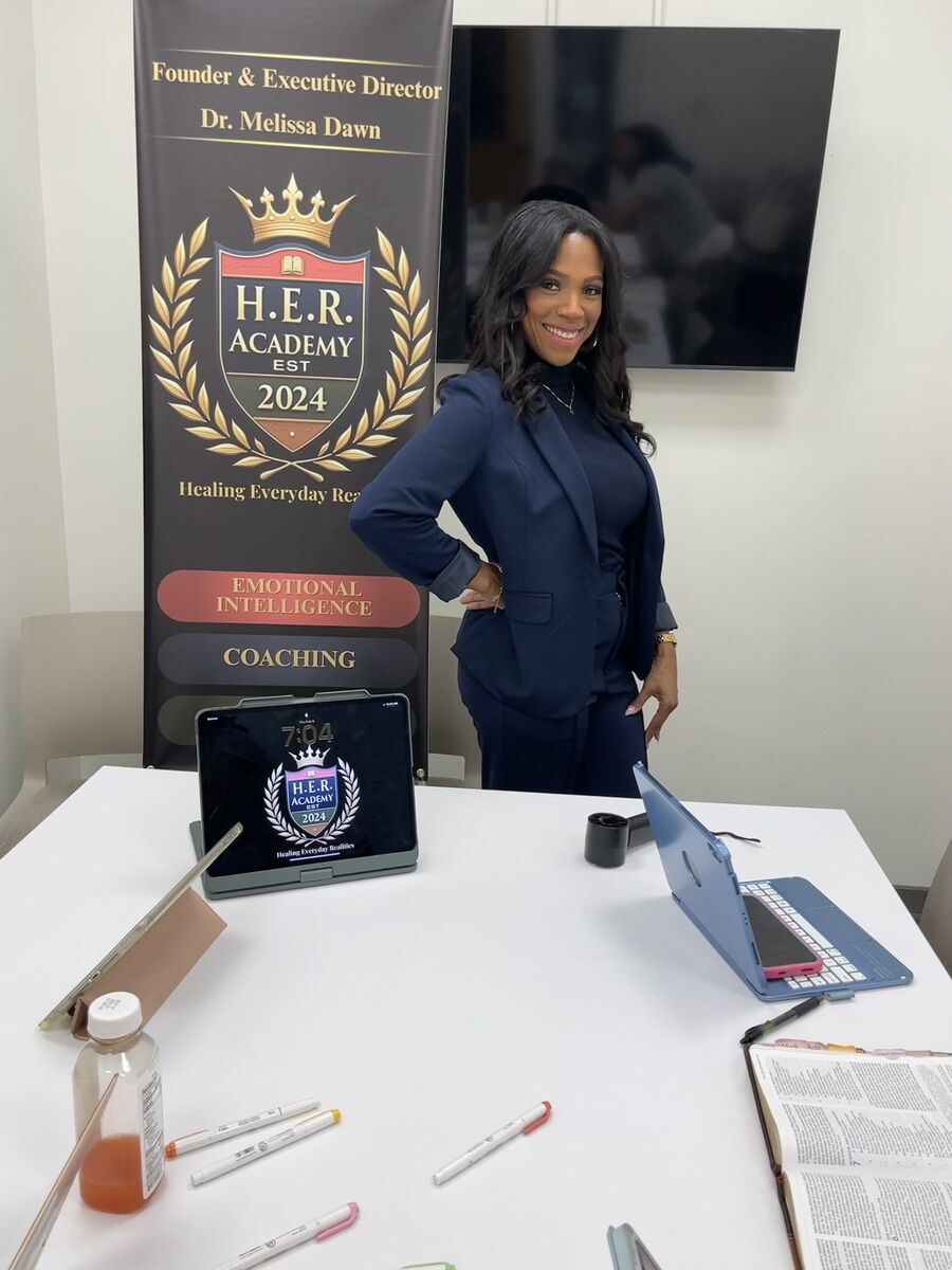Dr. Melissa Dawn standing beside an H.E.R. Academy banner at a coaching table set with laptops