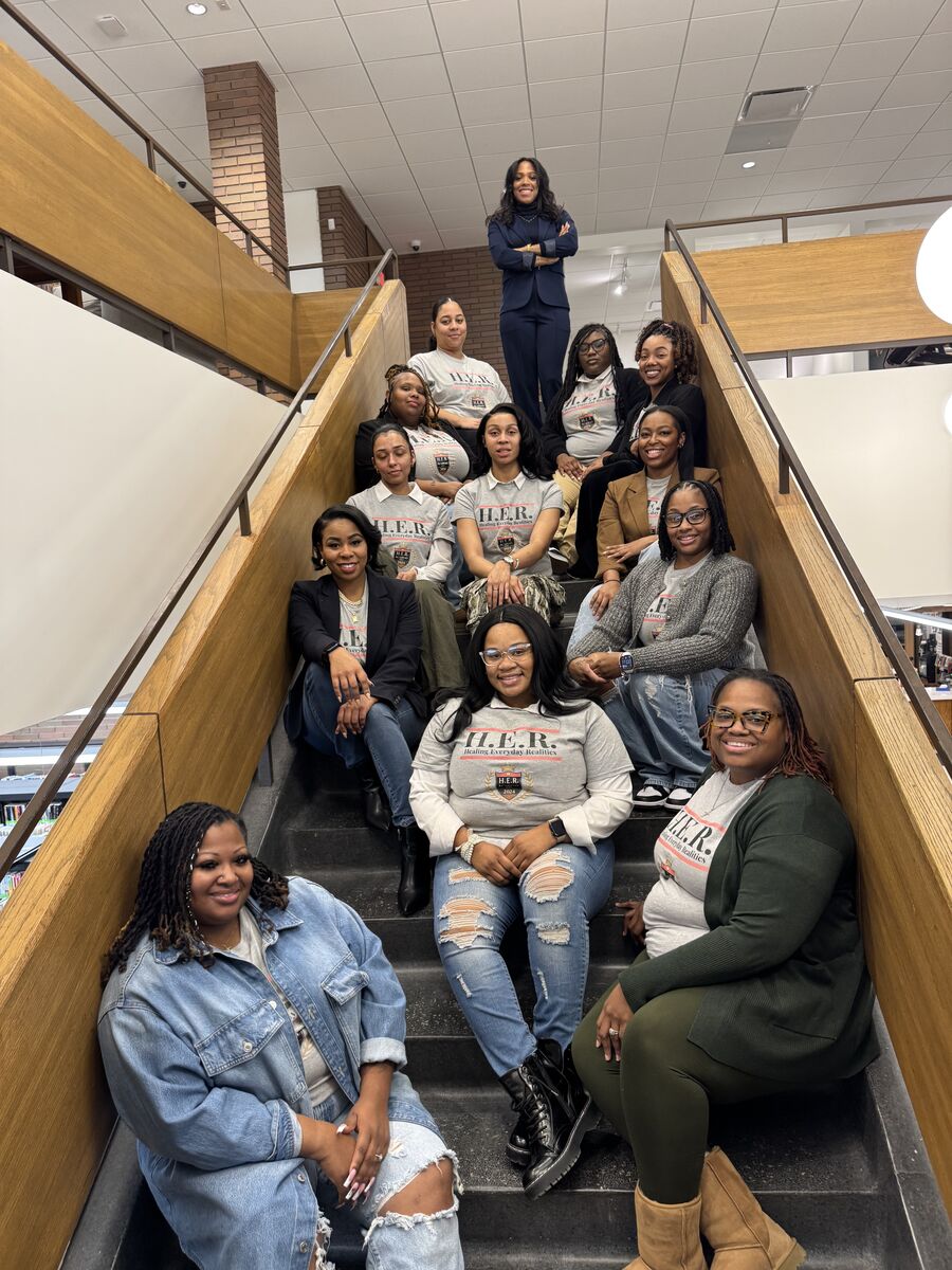 Members of H.E.R. Academy in matching tees, gathered together on a staircase after an event